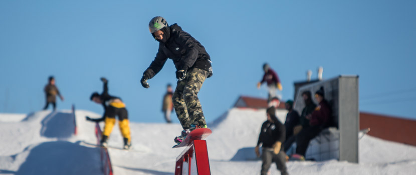 A snowboarder rides over a pipe feature. Several others snowboarders are behind him.
