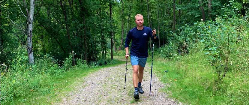 A man walks on a wooded trail using walking poles.