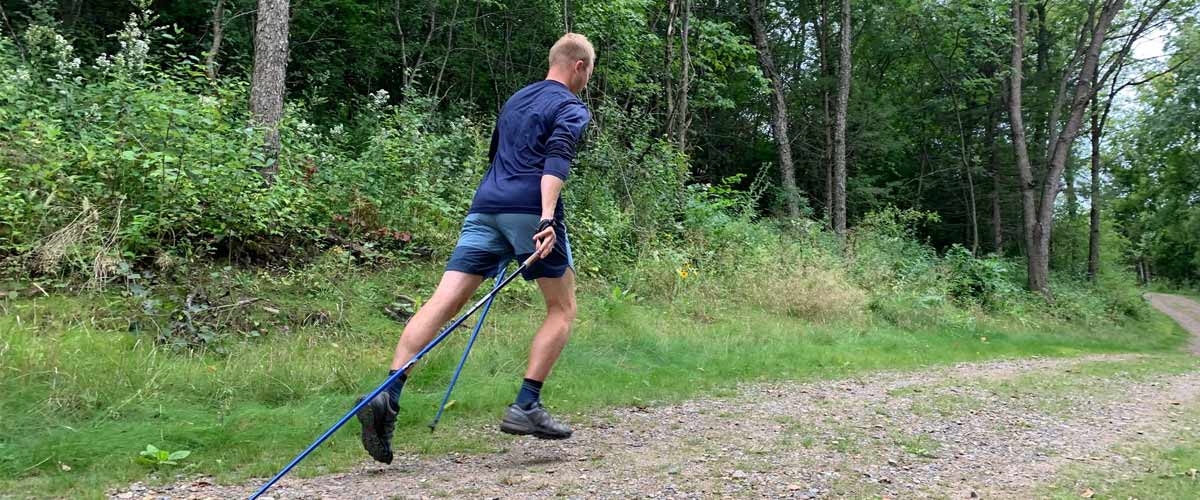 A man bounds up a trail using walking poles.