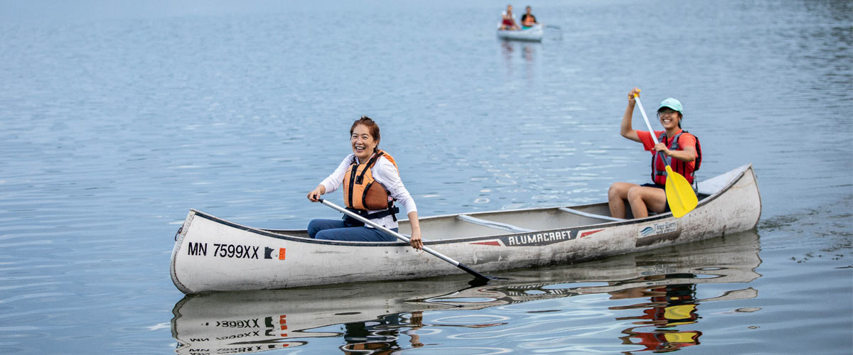 A younger woman and an older woman smile as they paddle a canoe.