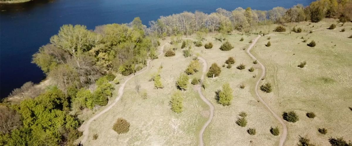 An aerial view of a mountain bike trail that winds past a lake through scrubby open areas.