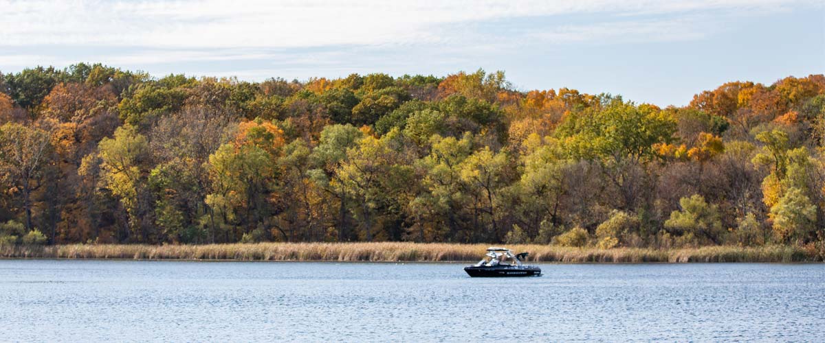A boat navigates a lake that is lined with colorful fall trees.