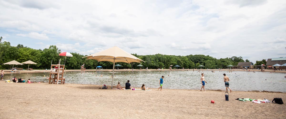 People sit around a swim pond lined with large umbrellas in the summer.