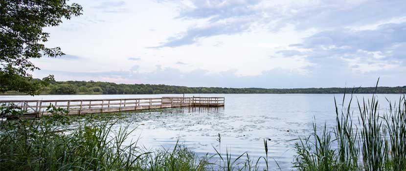 A fishing pier extends into a lake in the summer.