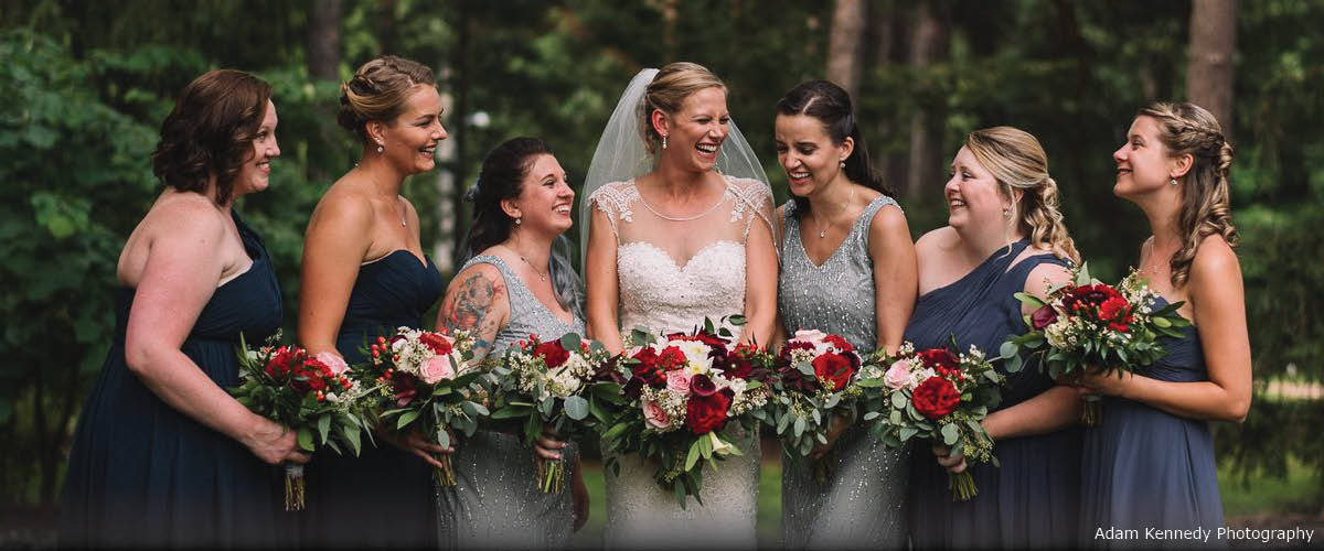 A bride stands in the middle of her bridesmaids in an outdoor setting.