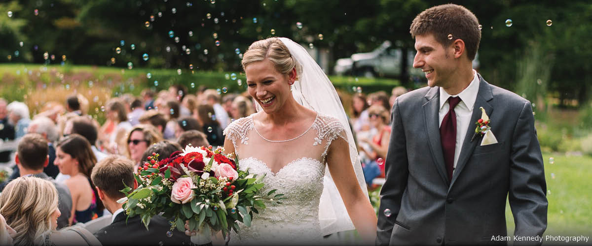 A couple smiles as they leave their ceremony while people blow bubbles.