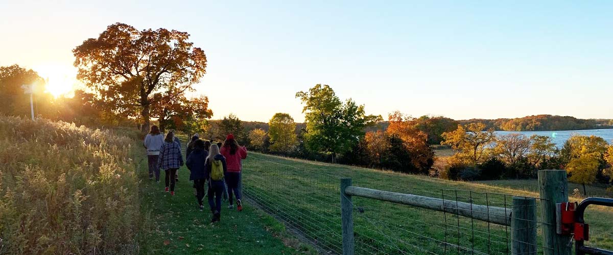 A group of teens walks along a pasture fence at sunset on a fall day.