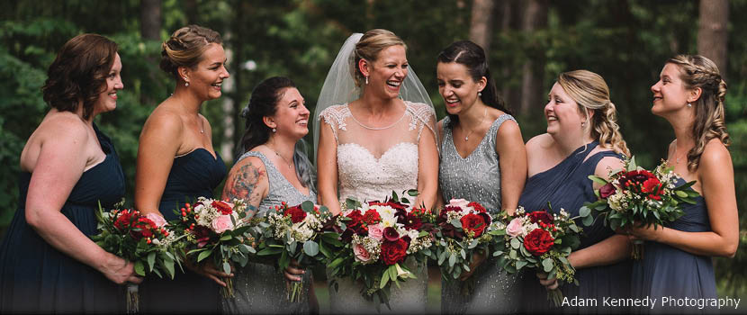 A bride and her bridesmaids smile as they hold bouquets in a row outside.
