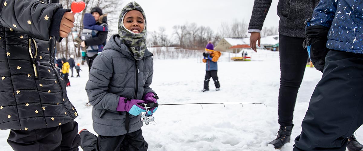 kid in winter gear ice fishing on a snowy lake