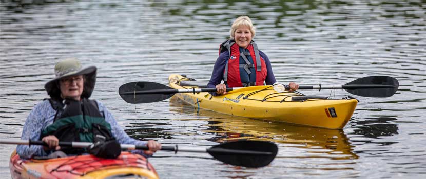 Two older women kayak on a lake.