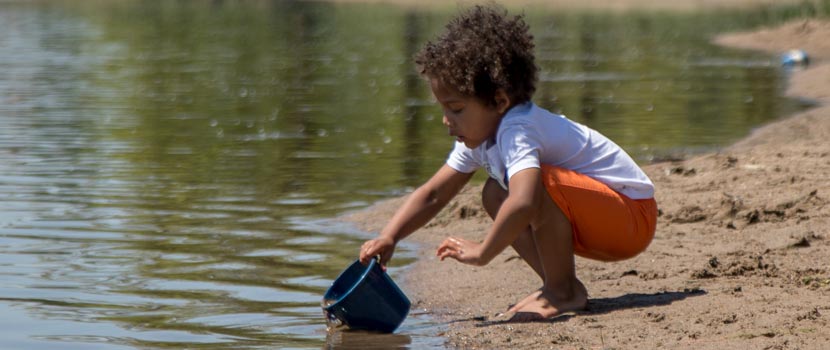 A boy dips a bucket in a lake while playing on a beach.