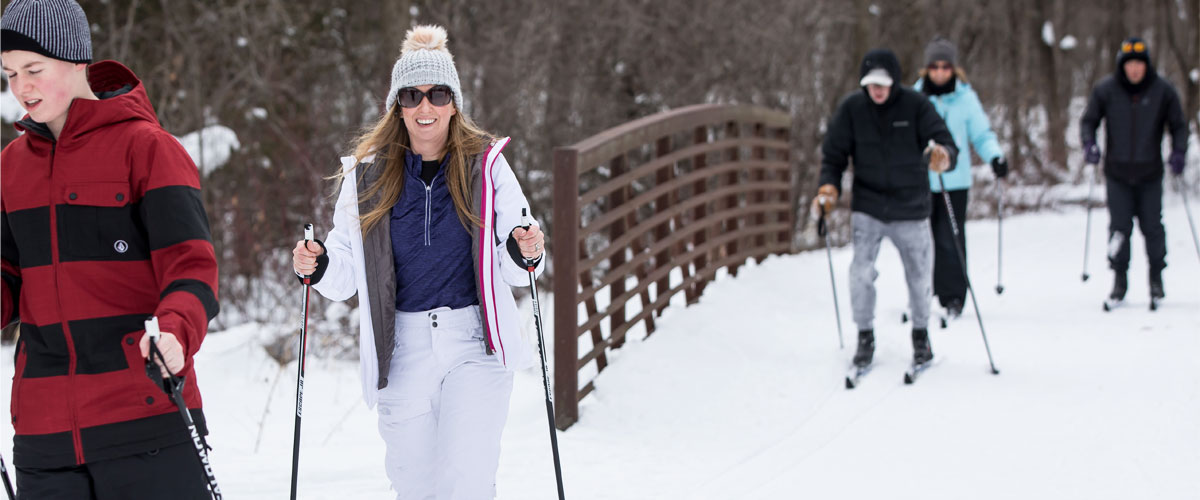 Several cross-country skiers cross a bridge in the winter.
