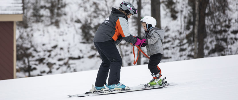 An instructor teaches a child how to downhill ski.