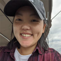 Chia Xiong wears a baseball cap and plaid shirt as she smiles at the camera.