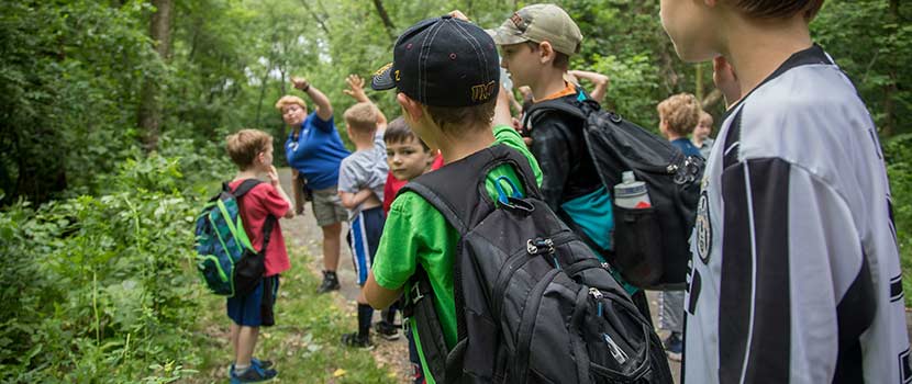 An instructor talking to a group of boys on a trail in the woods.