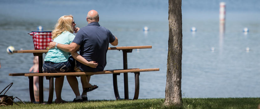 A man and woman sit at a picnic table on the banks of Fish Lake with their arms around each other.