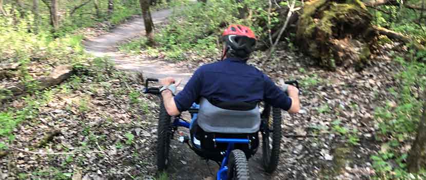 Adapted program participant Steve Laux rides his adapted handcycle with electronic assist on a dirt trail 