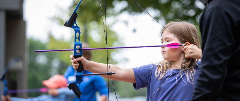 A girl pulls back a bow at an archery program.
