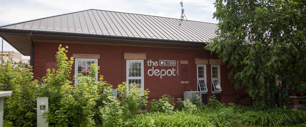 A view of The Depot coffee house, with green plants in front of it.