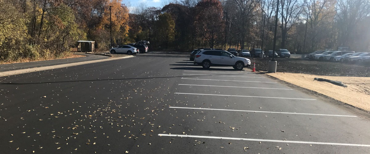 a freshly paved parking lot with cars, trees and sky in the background
