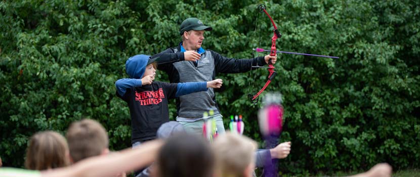 A Three Rivers instructor demonstrates archery form to a group of children.
