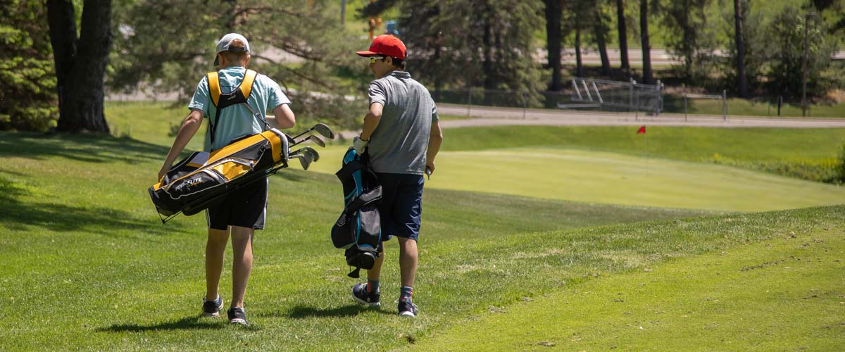 Two boys carry golf clubs on a golf course.