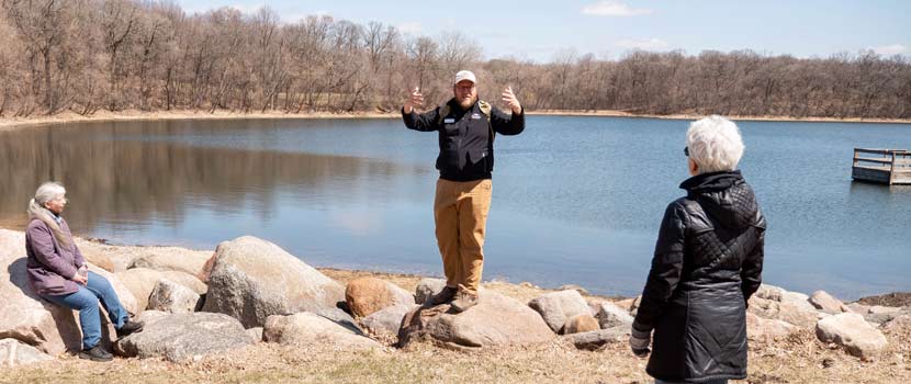 A Three Rivers Parks employee leads a program while standing on a rock next to Hyland Lake.
