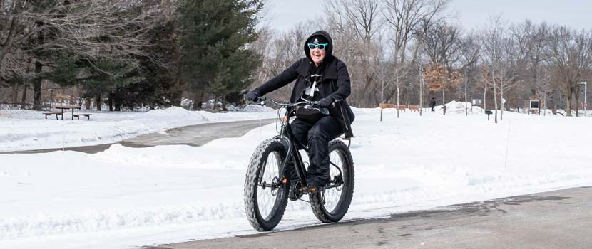 A person rides a fat bike down a snowy, paved trail.