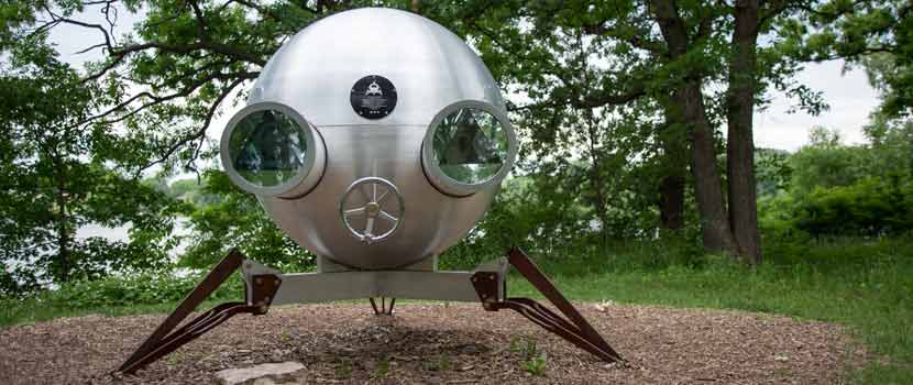 A metal sculpture on three legs that looks like a space ship.