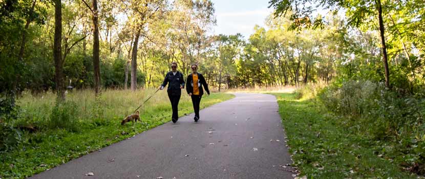 Two women walk a dog on a paved trail at Sochacki Park.