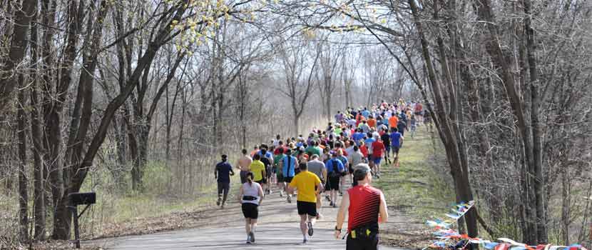 a group of runners running down a wooded trail in the spring.