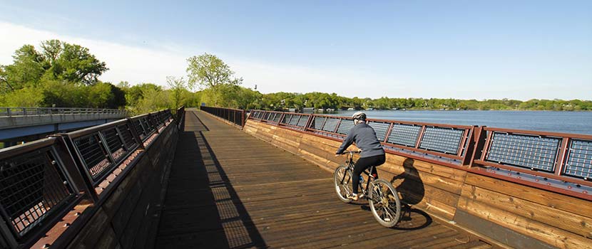 A man rides a bike across a wooden bridge in the fall.