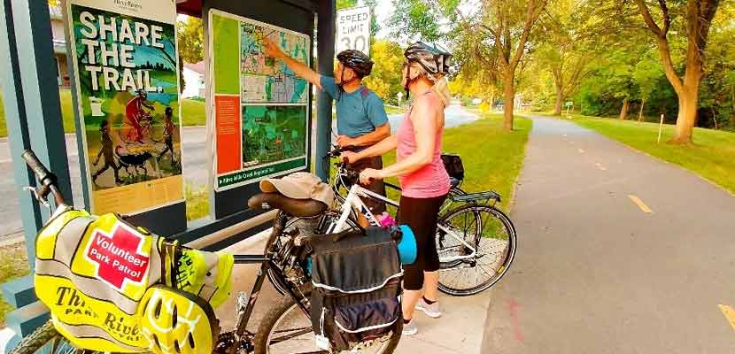two bikers looking at a trail map next to a paved trail