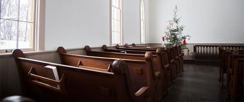 inside of an church with empty wooden pews facing a Christmas tree at the front