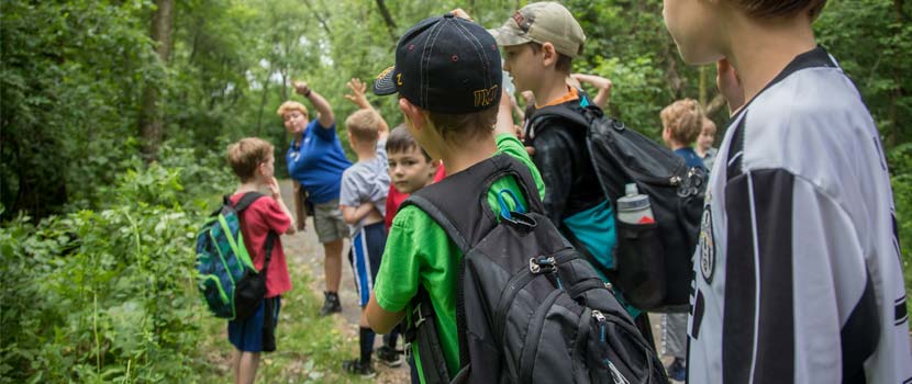 A group of boys stand in a line on a trail while a counselor counts them.