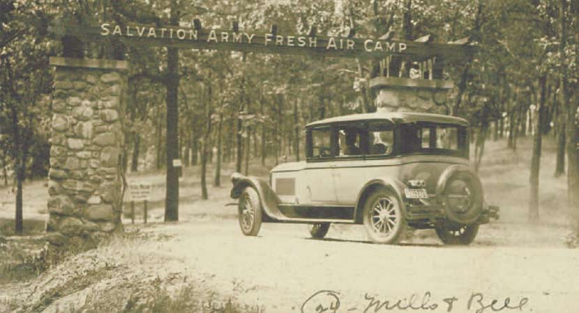 A historic photo of a car driving under a sign that says "Salvation Army Fresh Air Camp."