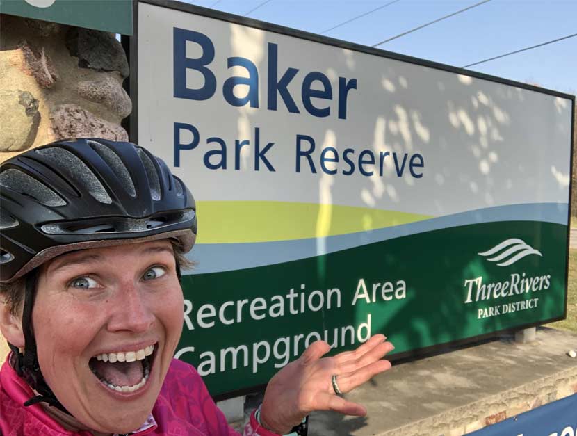 A woman takes a selfie in front of a park sign for Baker Campground.