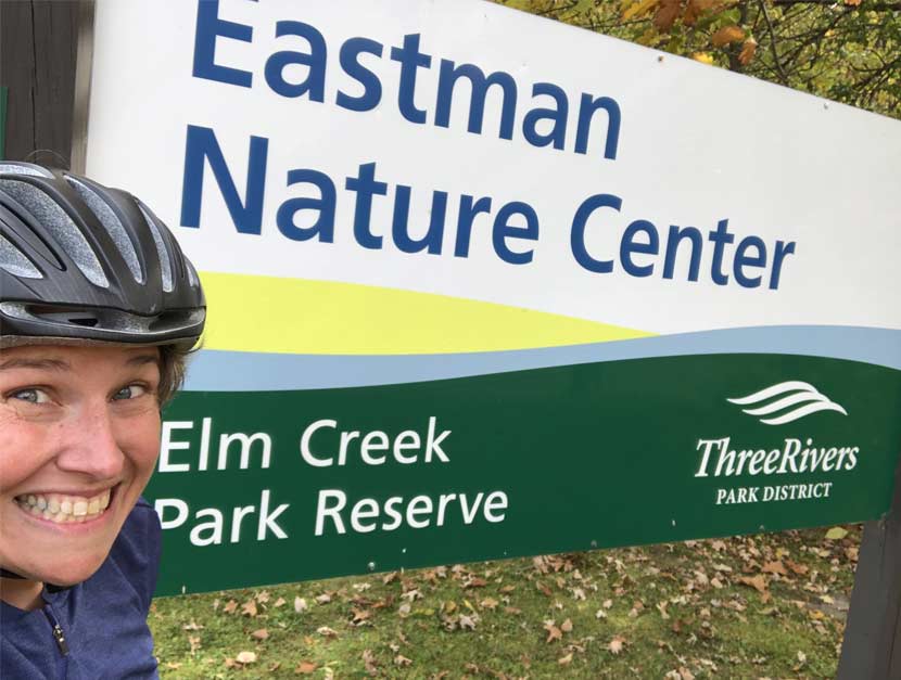 A woman takes a selfie in front of a park sign for Eastman Nature Center at Elm Creek Park Reserve.