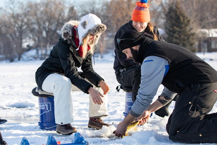 Three people pull a fish out of a lake while ice fishing.