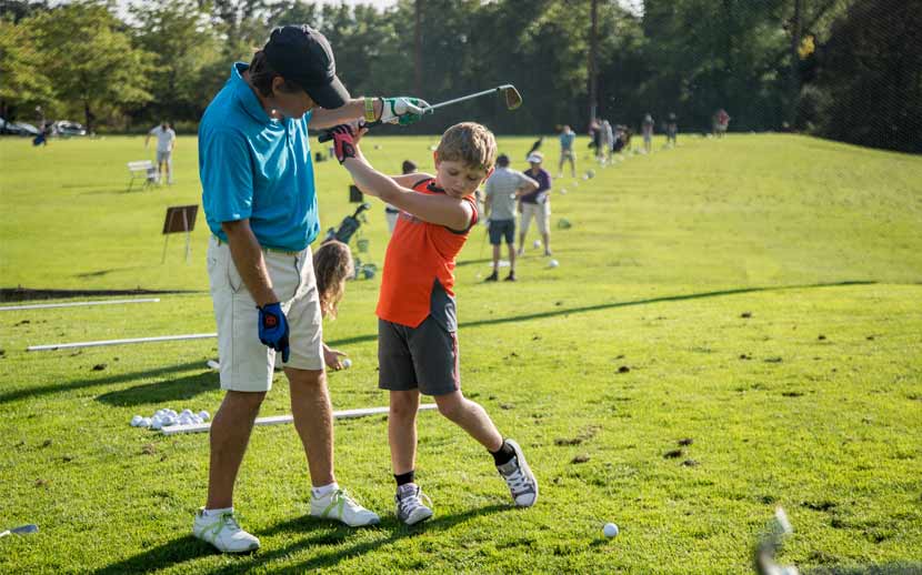 A man teaches a boy how to swing a golf club.