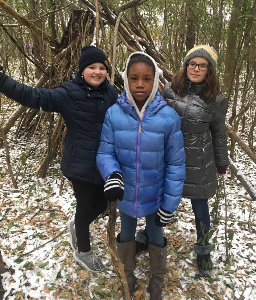 Three girls stand outside in the woods in the winter.