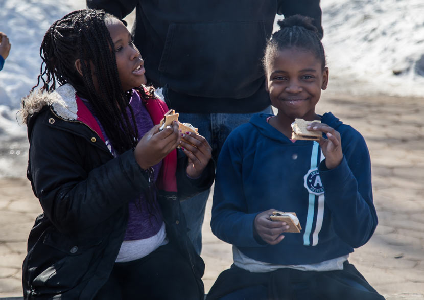 A girl grins as she eats a s'more on a bench at the Baker Outdoor Learning Center.