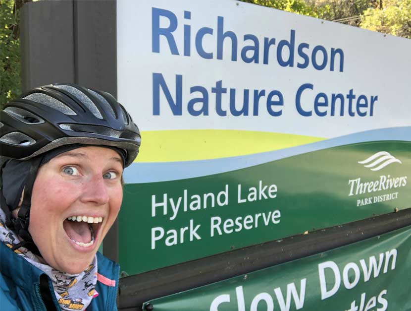 A woman takes a selfie in front of a park sign for Richardson Nature Center in Hyland Lake Park Reserve.