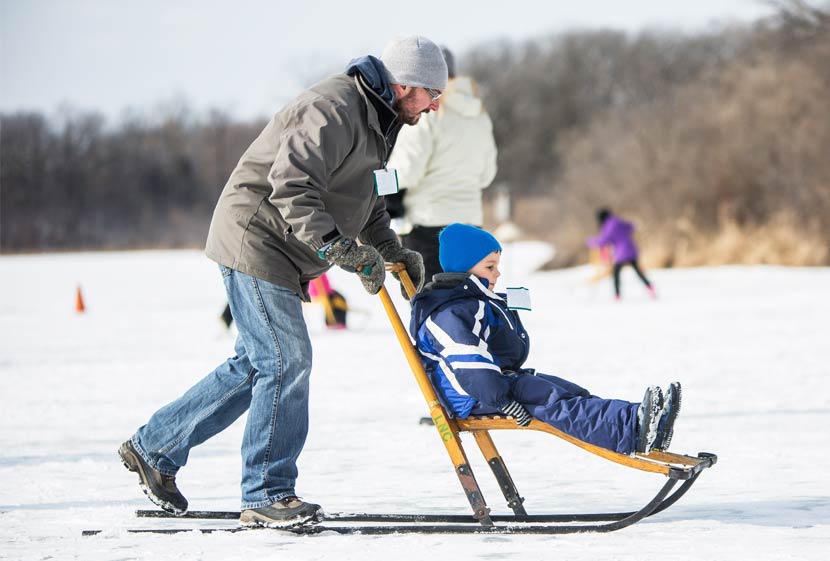A man pushes a small boy across a frozen lake on a kicksled.
