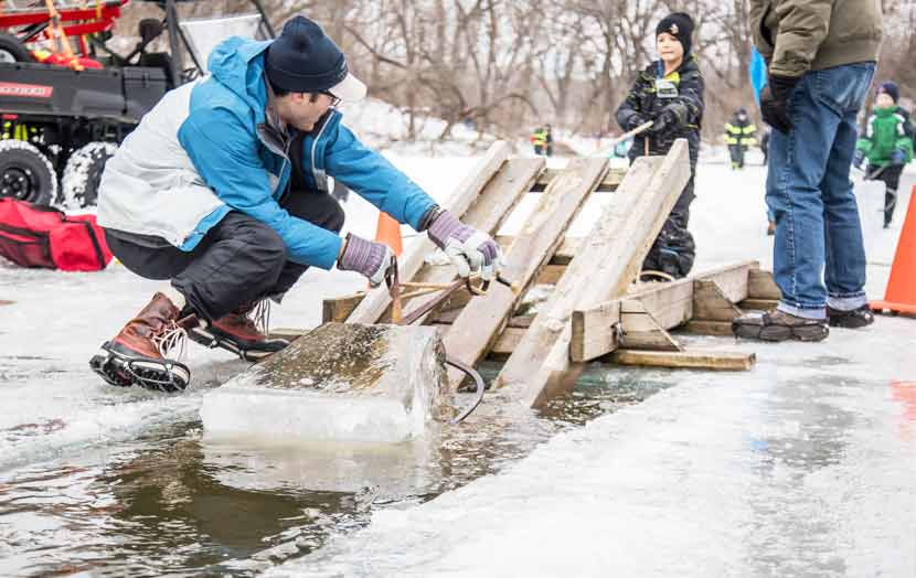 man and kid pulling large ice brick from water onto a pallet