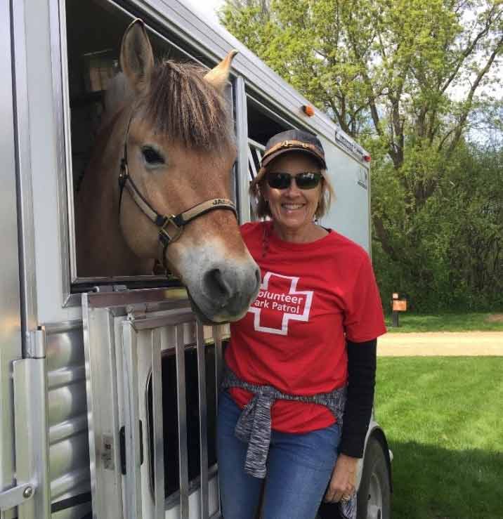 woman in a red volunteer shirt standing next to a horse trailer with her horse