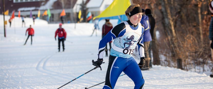 A woman competes in a cross-country ski race. Other racers can be seen in the distance behind her.