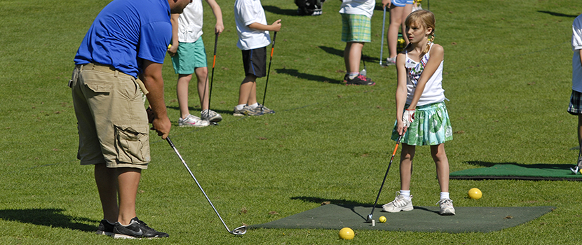 A young girl is instructed in golf