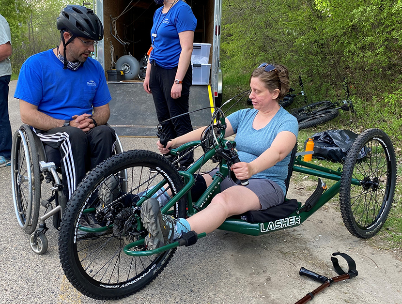 Sam Tabaka, Three Rivers Park District staff member, helps participant Annie Hickman get fitted and set up on a handcycle.