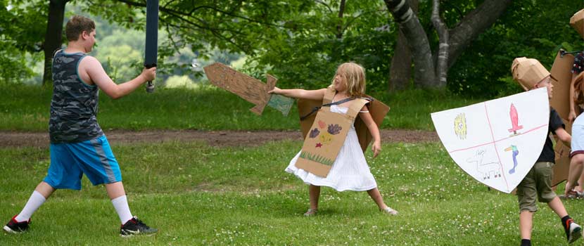 Kids at summer camp wearing pretend armor and holding a cardboard sword.